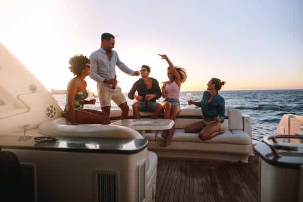 Group of happy friends having a boat party. Diverse men and women having drinks at sunset yacht party and dancing.